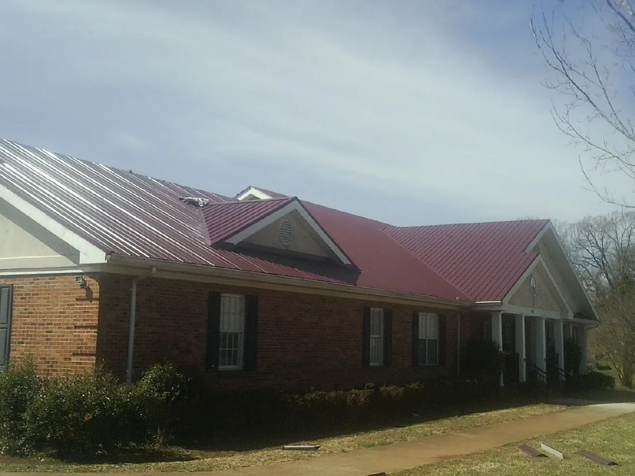 Red metal roof with gabled entries on a long brick building, from a Hail Damage Roof Repair job in Lummi Island