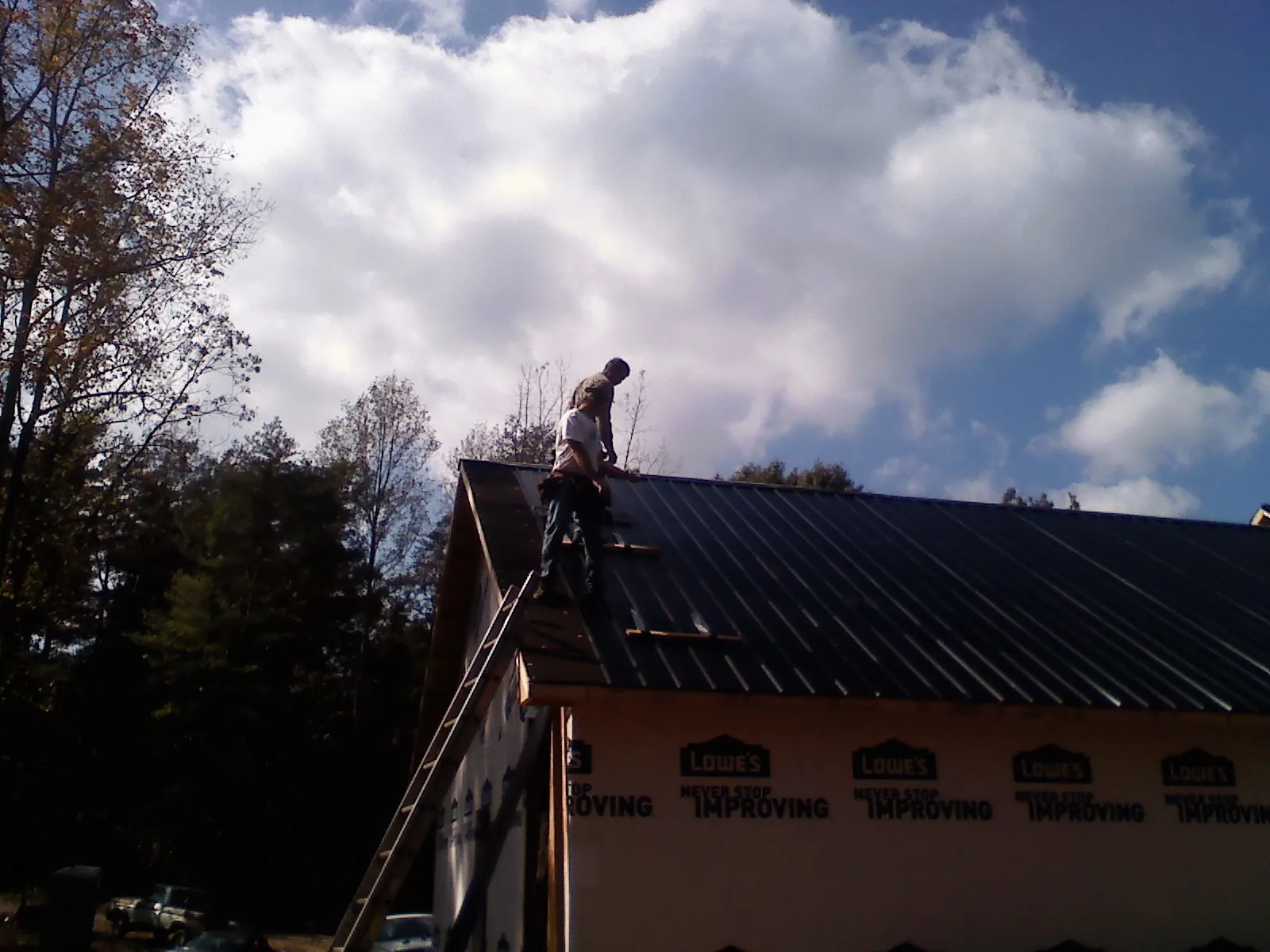 Roofer fastening dark metal panels high against a cloudy sky, from a Roof Inspection job in Lummi Island