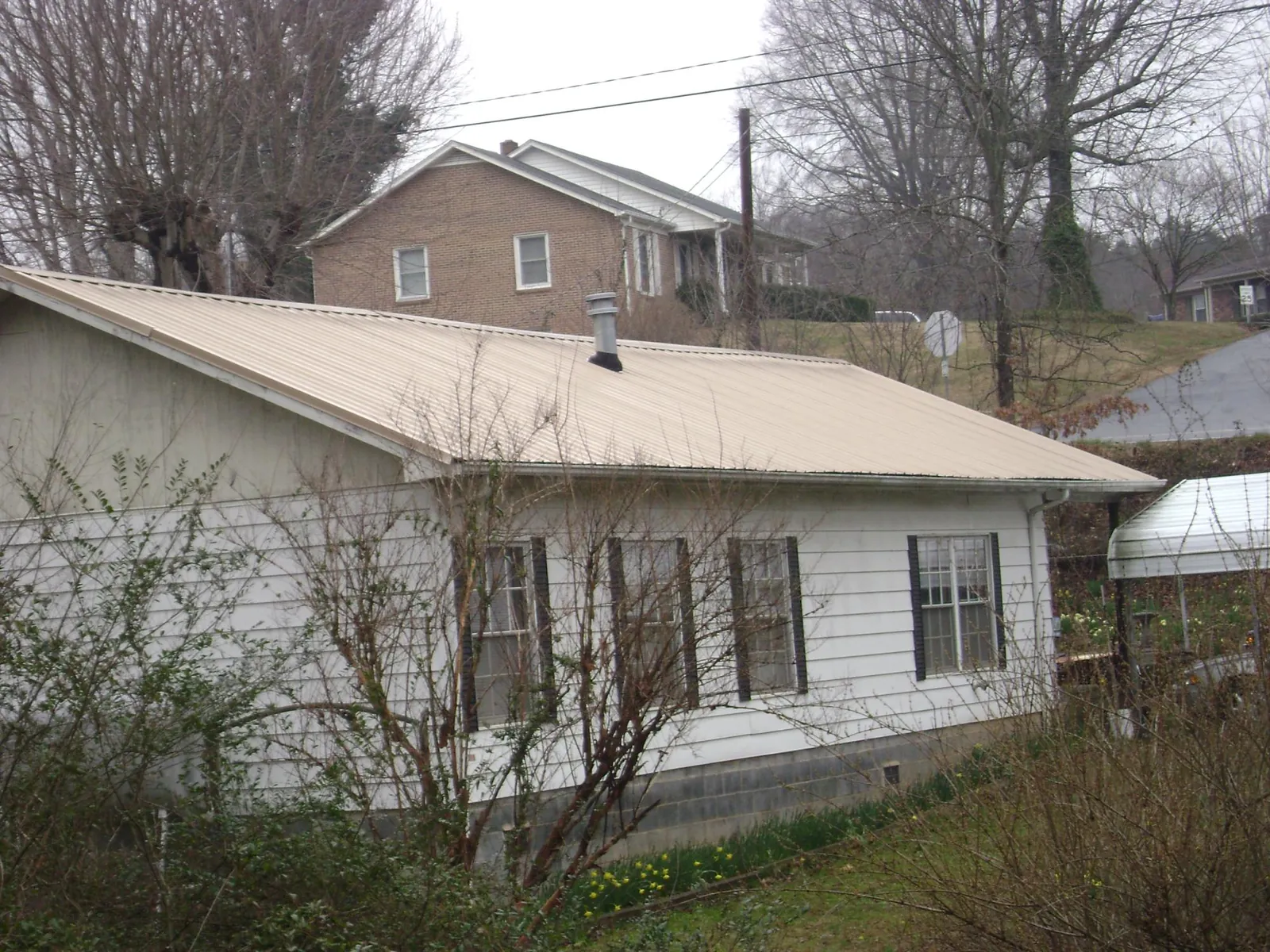 Tan metal roof on a white sided house set into a hillside — Commercial Roofing by Roofing Brothers in Lummi Island